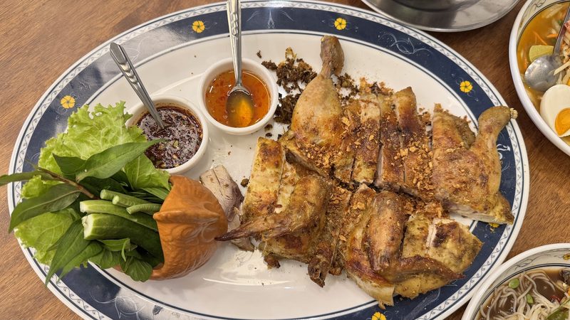 ไก่ย่างทั้งตัวแบบแผ่ หนังสีน้ำตาลเกรียม วางคู่ผักสดและน้ำจิ้ม