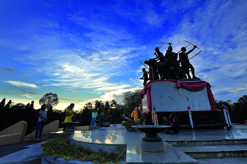 รูปปั้นวีรชนถือดาบและอาวุธบนฐานสูง ท้องฟ้ายามเย็น